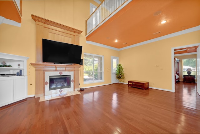 unfurnished living room with hardwood / wood-style flooring, ornamental molding, a towering ceiling, and a fireplace