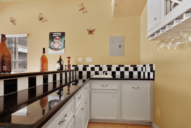 kitchen with white cabinets, light tile floors, sink, tasteful backsplash, and dark stone counters