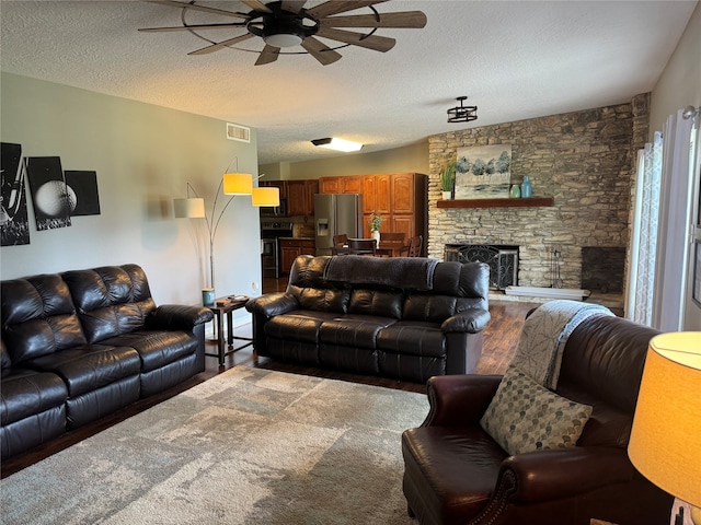 carpeted living room featuring a textured ceiling, ceiling fan, and a stone fireplace