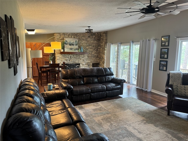 living room featuring plenty of natural light, a stone fireplace, dark hardwood / wood-style floors, and a textured ceiling