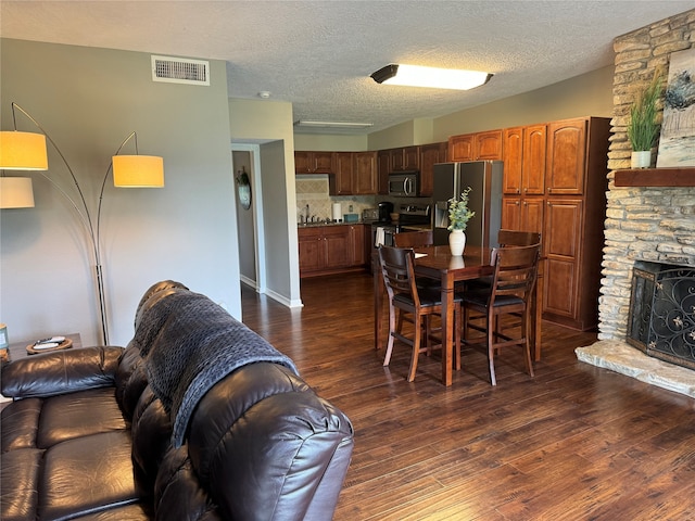 dining area with a textured ceiling, sink, a stone fireplace, and dark wood-type flooring