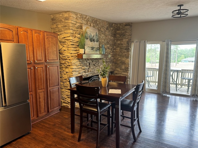 dining area featuring a textured ceiling, dark wood-type flooring, and a stone fireplace