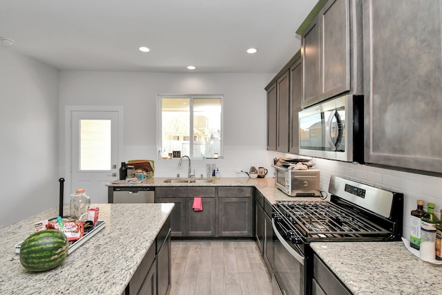 kitchen featuring backsplash, sink, light stone countertops, light wood-type flooring, and appliances with stainless steel finishes