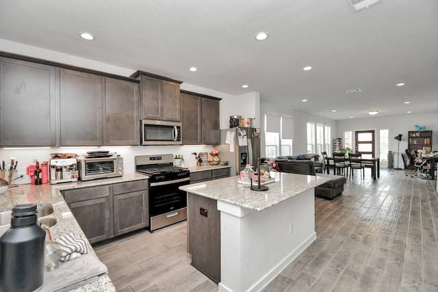 kitchen with light stone countertops, light wood-type flooring, and appliances with stainless steel finishes