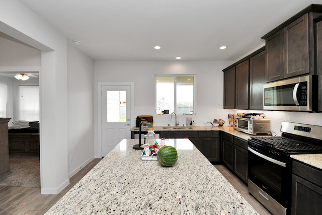 kitchen with appliances with stainless steel finishes, tasteful backsplash, light hardwood / wood-style floors, light stone counters, and dark brown cabinetry