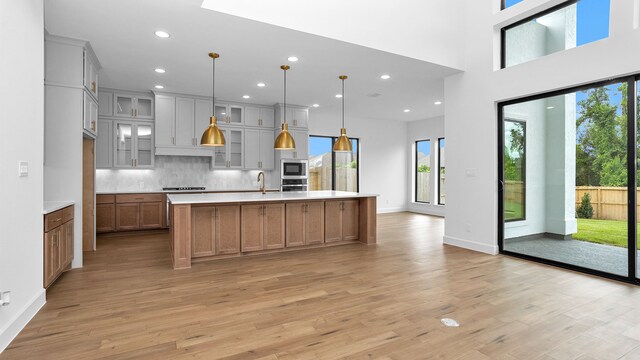 kitchen with decorative light fixtures, a large island with sink, light wood-type flooring, and plenty of natural light