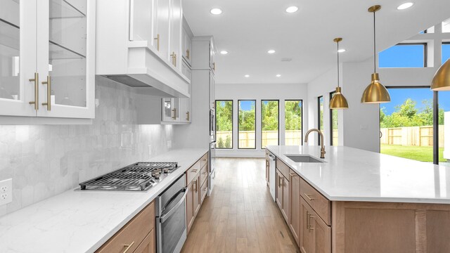 kitchen featuring light stone countertops, stainless steel appliances, pendant lighting, light hardwood / wood-style flooring, and white cabinetry