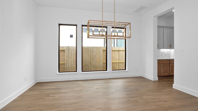 unfurnished dining area featuring plenty of natural light, light hardwood / wood-style floors, and an inviting chandelier