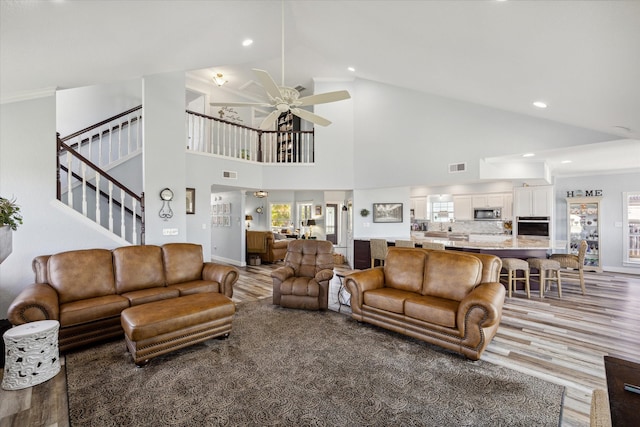 living room with hardwood / wood-style floors, ceiling fan, and high vaulted ceiling