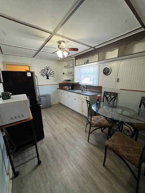 kitchen featuring ceiling fan, light hardwood / wood-style floors, white cabinetry, sink, and black refrigerator