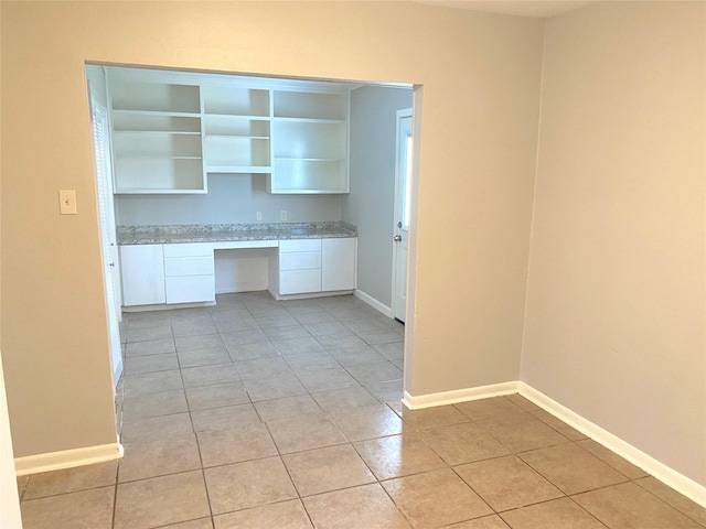 kitchen featuring light tile patterned floors, built in desk, and white cabinetry