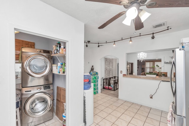 laundry area with stacked washer / drying machine, ceiling fan with notable chandelier, and light tile floors