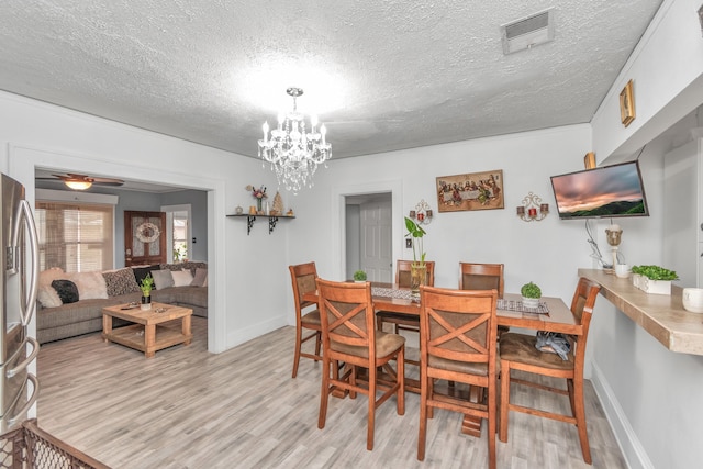 dining room featuring ceiling fan with notable chandelier, light hardwood / wood-style floors, and a textured ceiling