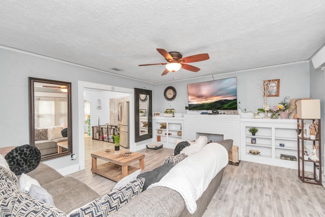 living room featuring a brick fireplace, ceiling fan, a textured ceiling, and light wood-type flooring