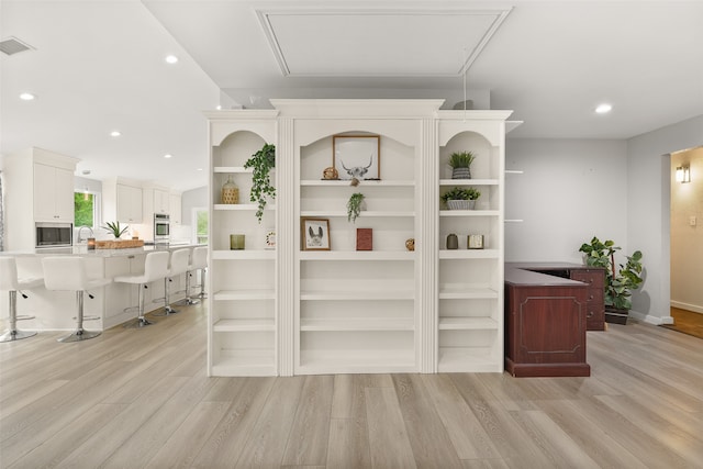 bar with stainless steel microwave, white cabinets, and light hardwood / wood-style flooring