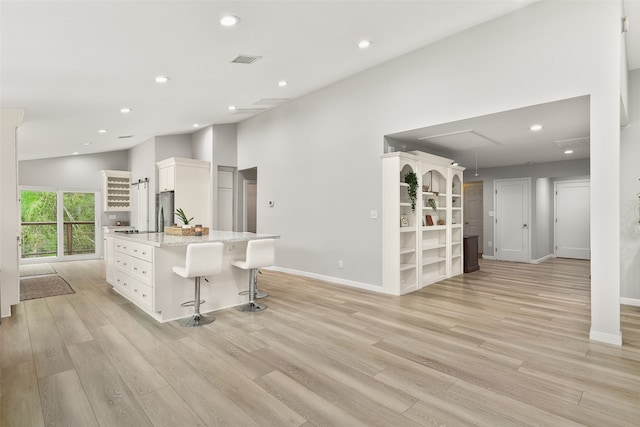 kitchen with white cabinets, stainless steel appliances, a center island, a breakfast bar area, and light wood-type flooring