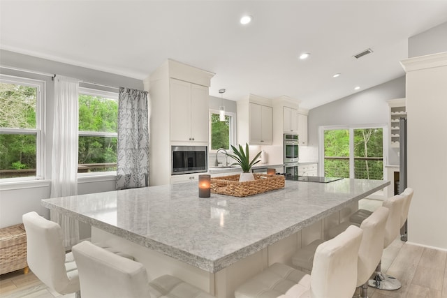 kitchen featuring plenty of natural light, light wood-type flooring, decorative light fixtures, lofted ceiling, and a spacious island