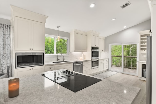 kitchen with pendant lighting, light hardwood / wood-style flooring, vaulted ceiling, sink, and stainless steel appliances