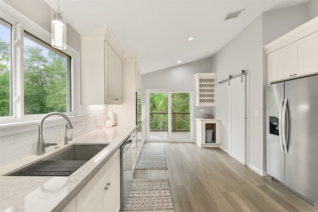 kitchen with a barn door, vaulted ceiling, sink, stainless steel appliances, and white cabinetry