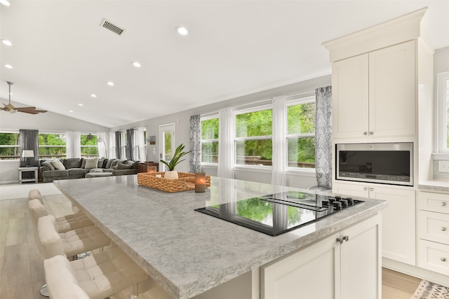 kitchen featuring black electric cooktop, ceiling fan, white cabinets, vaulted ceiling, and light hardwood / wood-style flooring