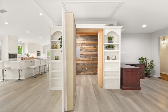 bar with stainless steel microwave, white cabinets, and light wood-type flooring