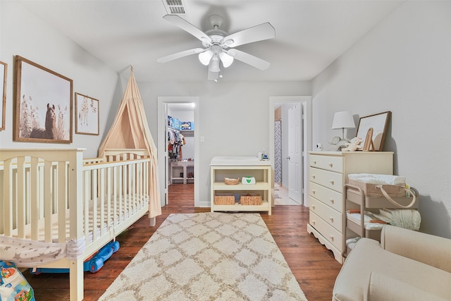 bedroom featuring ceiling fan, a closet, a nursery area, dark wood-type flooring, and a walk in closet