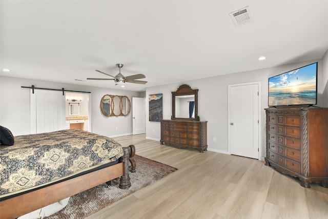 bedroom with a barn door, ensuite bath, light wood-type flooring, and ceiling fan