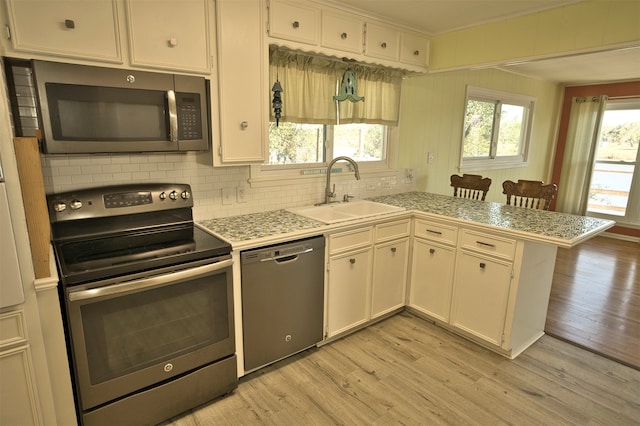 kitchen with kitchen peninsula, appliances with stainless steel finishes, sink, and light hardwood / wood-style flooring