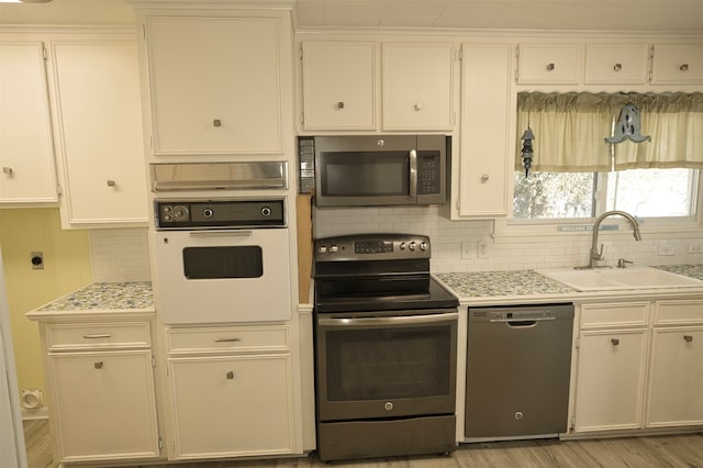 kitchen featuring white cabinetry, sink, appliances with stainless steel finishes, light wood-type flooring, and decorative backsplash