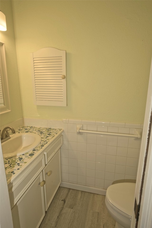 bathroom with hardwood / wood-style flooring, vanity, toilet, and tile walls