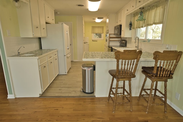 kitchen featuring stainless steel appliances, a breakfast bar area, white cabinets, and light hardwood / wood-style flooring