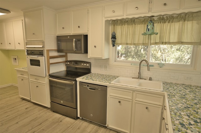 kitchen featuring stainless steel appliances, sink, tasteful backsplash, light hardwood / wood-style flooring, and white cabinets