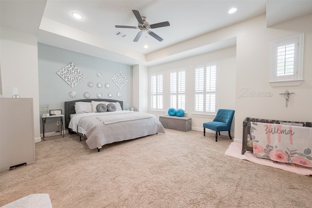 bedroom featuring light carpet, a tray ceiling, ceiling fan, and multiple windows