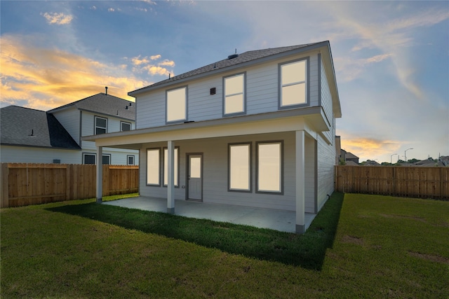 back house at dusk with a patio and a yard