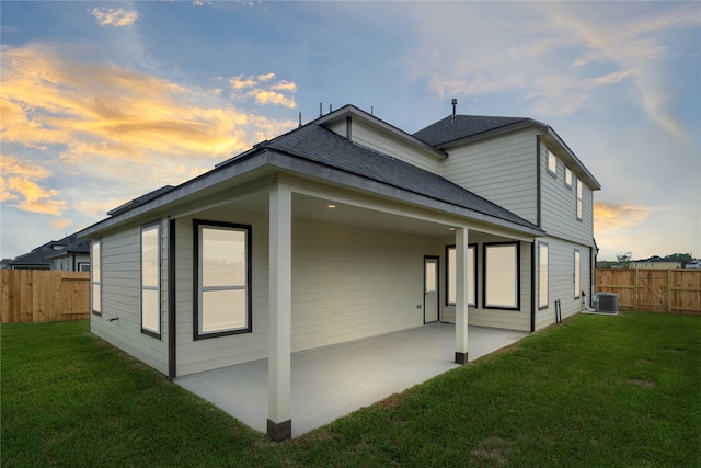 back house at dusk featuring cooling unit, a patio, and a yard