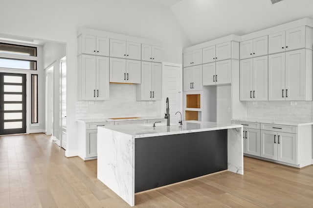 kitchen with light wood-type flooring, backsplash, a center island with sink, and light stone counters