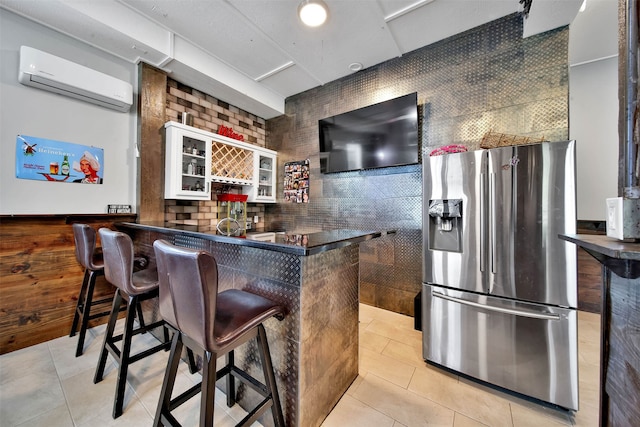 bar with a wall unit AC, light tile floors, backsplash, white cabinetry, and stainless steel fridge with ice dispenser