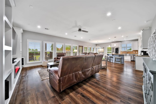 living room featuring ceiling fan, a wealth of natural light, and dark wood-type flooring