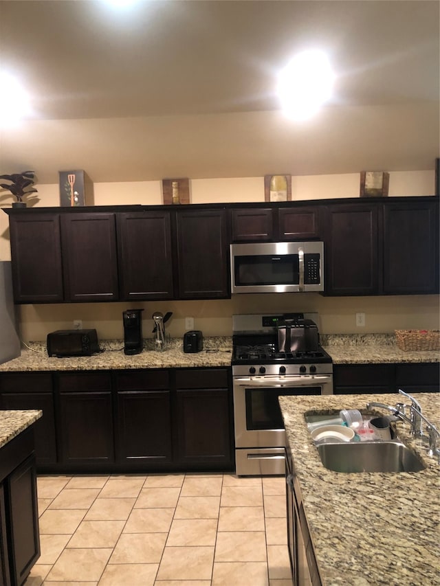 kitchen with stainless steel appliances, light tile floors, sink, and light stone counters