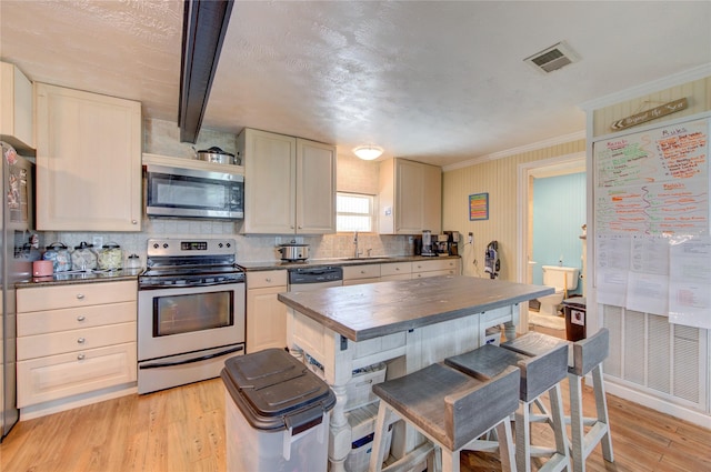 kitchen featuring sink, light hardwood / wood-style flooring, ornamental molding, stainless steel appliances, and cream cabinets