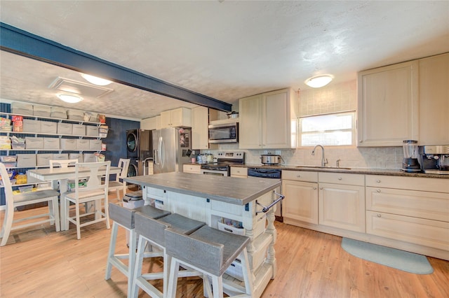 kitchen with stacked washer / drying machine, stainless steel appliances, light hardwood / wood-style floors, sink, and cream cabinetry