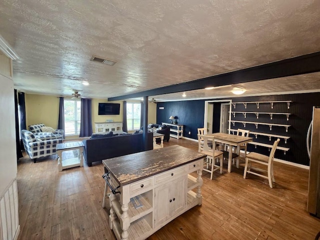 kitchen with white cabinets, beamed ceiling, ceiling fan, stainless steel refrigerator, and hardwood / wood-style flooring