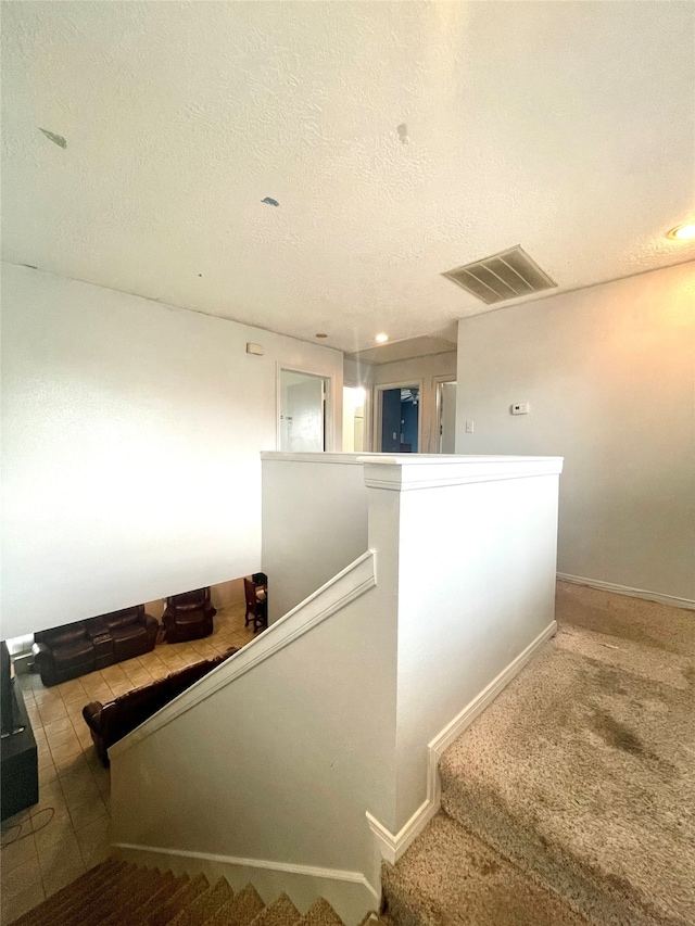 stairway featuring carpet flooring and a textured ceiling