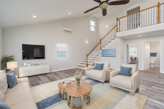 living room with high vaulted ceiling, ceiling fan, a wall unit AC, and light wood-type flooring