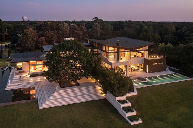 back house at dusk featuring a lawn and a patio area