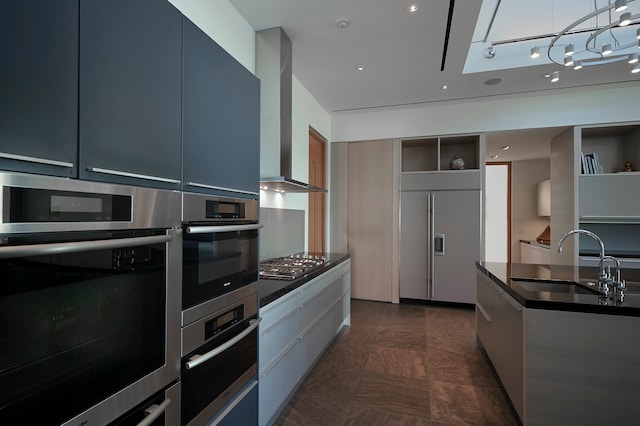 kitchen with appliances with stainless steel finishes, dark tile flooring, wall chimney exhaust hood, sink, and pendant lighting