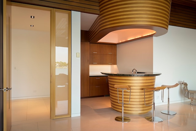 bar featuring sink, dark stone countertops, and light tile floors