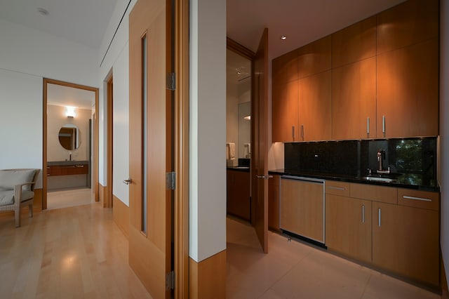 kitchen featuring dishwasher, tasteful backsplash, dark stone counters, sink, and light tile floors