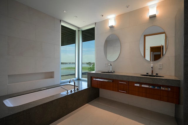 bathroom with vanity with extensive cabinet space, a bathtub, tile floors, tile walls, and double sink