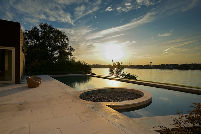 pool at dusk with a patio area and a water view